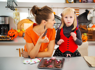 Girl in bat costume with smiling mother eating Halloween cookies