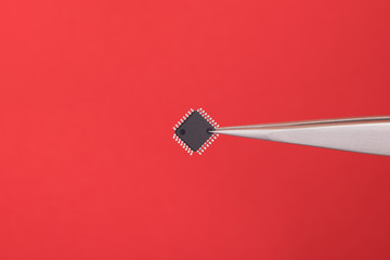 SMD Bauteil und Pinzette vor rotem Hintergrund