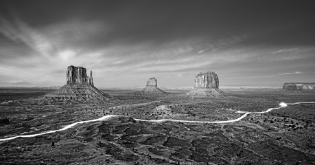 Black and white photo of Monument Valley with car lights trails at night, USA.