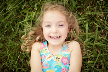 Top view portrait of a smiling shy little girl lying on green grass
