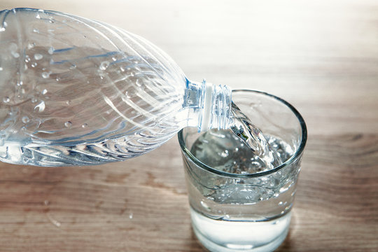 bottiglia di plastica che versa acqua in un bicchiere trasparente di vetro