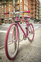 Fototapeta na wymiar Pink bicycle on a quiet street in SOHO, New York with a brick building in the background