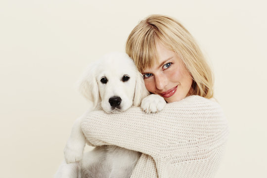 Blond woman hugging puppy in studio, portrait