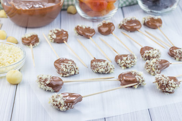 Making apricot and prunes lollipops, covered with chocolate and macadamia nuts