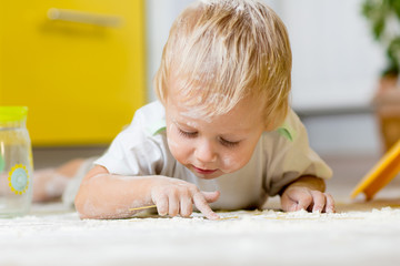 Little child laying on very messy kitchen floor, covered in