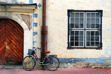 Fototapeta na wymiar Bicycle stands at the gate in an old house with a square window