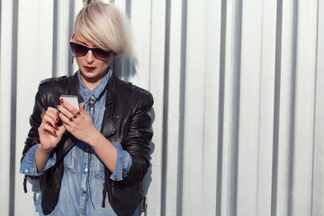 young punk style blond lady leaning on wall and using her mobile phone