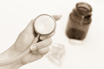 hand holding stethoscope on blur capsule pouring from glass bottle ,image in vintage tone