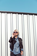 Fototapeta premium young punk style blond lady leaning on wall and using her mobile phone