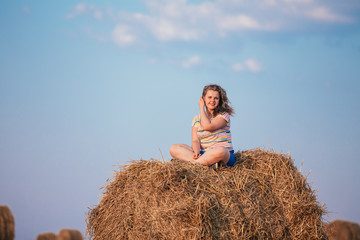 Naklejka na ściany i meble Beautiful Plus Size Girl Sitting On A Haystack And Smiling. Summ