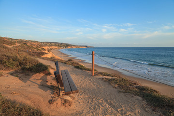 Naklejka premium Bench along an outlook with a view at sunset of Crystal Cove Beach, Newport Beach and Laguna Beach line in Southern California
