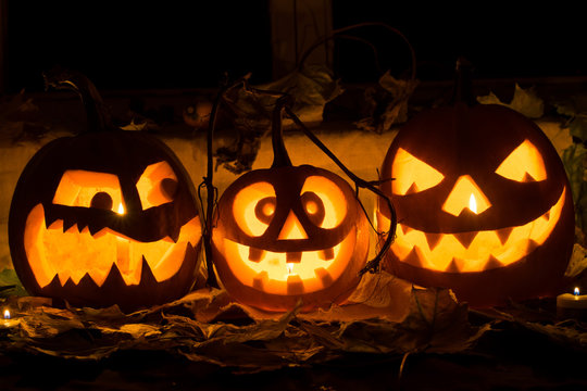 Photo of three pumpkins for Halloween. Embittered, cheerful with a smile and evil pumpkin against autumn leaves and candles