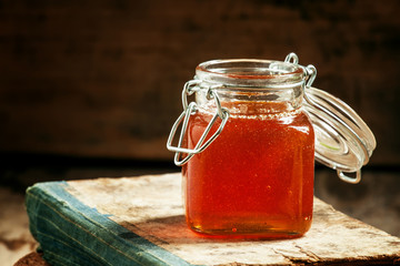 Dark honey from alpine herbs in a glass jar with a lid on old wo