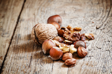 Fototapeta premium Hazelnuts and walnuts on old wooden table, toned image, selectiv