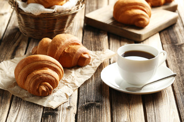 Tasty croissants with cup of coffee on brown wooden background