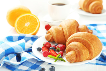Fresh tasty croissants with berries on white wooden background