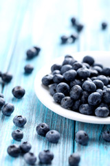 Tasty blueberries in plate on a blue wooden table