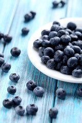 Tasty blueberries in plate on a blue wooden table