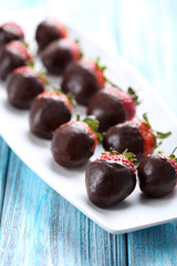 Fresh strawberries dipped in dark chocolate on blue wooden backg