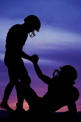 Tuinposter silhouette of one football player helping another up © Poulsons Photography