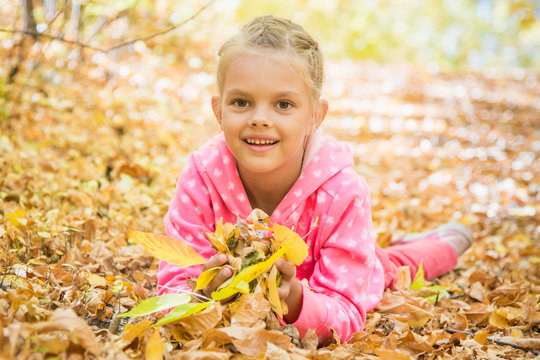 Six year old girl lying on the yellow fallen leaves
