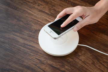 a hand putting mobile phone on a wireless charger, modern equipm - obrazy, fototapety, plakaty