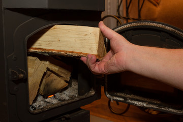 solid fuel burning stoves. man puts a firewood in a wood stove. The stove in a country house. The interior of a country house.