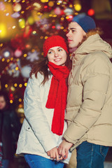 Christmas and people concept - young winter couple over christmas tree outdoor