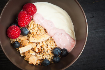 A bowl of healthy breakfast muesli with yogurt and topped with fresh raspberries, blueberries, chia seeds and coconut shavings.