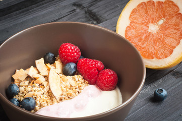 A bowl of healthy breakfast fruit muesli with yogurt and topped with fresh strawberries, sliced melon, goji berries, blueberries and coconut shavings.