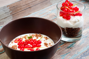 A bowl of healthy breakfast muesli with yogurt and topped with fresh red berries. Served with a side of crunchy granola layered with yogurt in a glass.