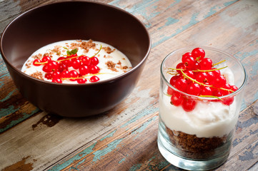 A bowl of healthy breakfast muesli with yogurt and topped with fresh red berries. Served with a side of crunchy granola layered with yogurt in a glass.