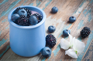 Healthy breakfast of a mixed berry smoothie milkshake made from blended blueberries and blackberries  with yogurt. Served in a blue ceramic pot on a rustic wooden table.
