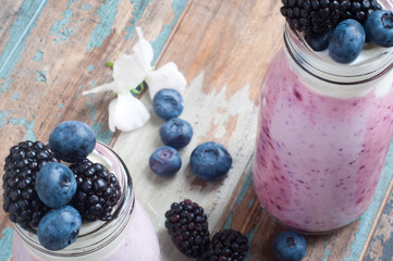 Healthy breakfast of a mixed berry smoothie milkshake made from blended blueberries and blackberries  with yogurt. Served in a glass bottle on a rustic wooden table.