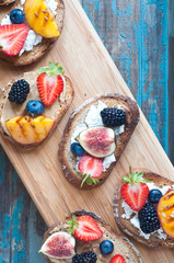 Healthy fruit topped open sandwich of Wholemeal rye bread with strawberry, blackberry, grilled peach and fig. Served on a wooden board.