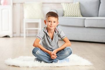 Little boy sitting on carpet, on home interior background