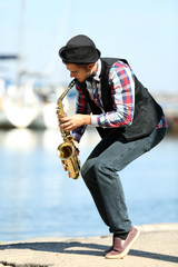 Young man playing on saxophone on the riverside
