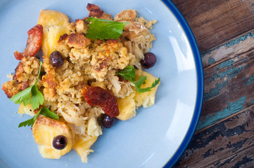 Bacalhau broa. A Portuguese Brazilian dish of salt cod baked with crumbled corn bread, olive oil and olives. Garnished with sun dried tomatoes and parsley.