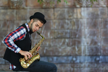 Handsome young man plays sax on stone wall background
