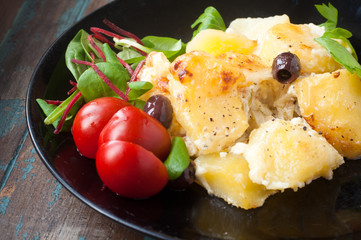 Bacalhau com natas. A Portuguese Brazilian dish of salt cod cooked with potatoes, cream and olives. Served with tomatoes and fresh salad leaves.