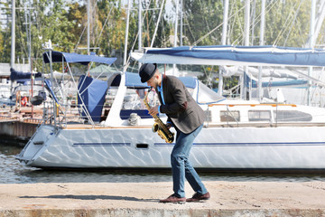 Fototapeta premium Handsome man plays sax in front of yacht