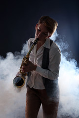 Naklejka na ściany i meble Attractive woman plays saxophone on dark background in the smoke