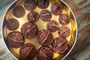 Freshly baked and decorated chocolate muffins arranged in a cake tin with a gold background.