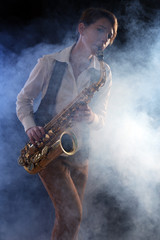 Plakat Attractive woman plays saxophone on dark background in the smoke