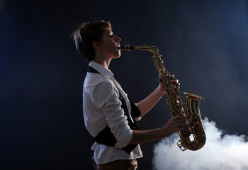 Fototapeta na wymiar Attractive woman plays saxophone on dark background