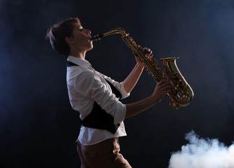 Fototapeta na wymiar Attractive woman plays saxophone on dark background