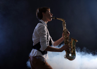 Obraz na płótnie Canvas Attractive woman plays saxophone on dark background