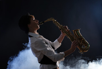 Fototapeta na wymiar Attractive woman plays saxophone on dark background in the smoke