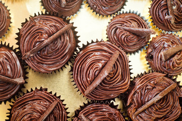 Freshly baked and decorated chocolate muffins arranged in a cake tin with a gold background. The cakes look like mechanical cogs or gears in a gearbox.