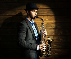 Elegant saxophonist plays jazz on wooden background